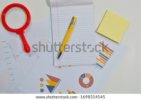 notepad, graph, pens and lens on a table indicating a work area or a work desk top