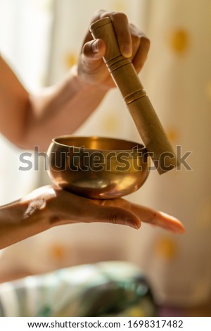 Close-up of of a young yogin woman holding a tibetan bowl and a stick in the beautiful and gentle light of morning during a yoga session, creating a meditative state through music. Royalty-Free Stock Photo #1698317482