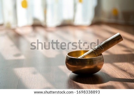 Tibetan golden bowl with a wooden stick sitting on the floor in the soft light of morning. Peaceful meditation music for mind and positive energy through healing sounds. Royalty-Free Stock Photo #1698338893