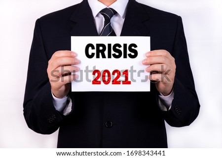 A businessman is holding a tablet with the text Crisis 2021 in front of him in his hands. Business concept