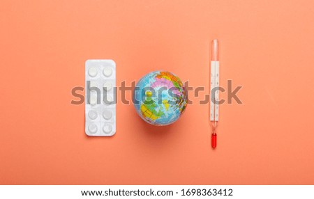 Pandemic outbreak or global warming concept. Globe, thermometer and blister of pills on orange  background. Top view