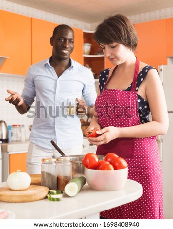 Happy African American male and Caucasian female making dinner together in kitchen