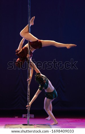 The duo of a girl athlete gymnasts show a pair acrobatic performance on the pylon.