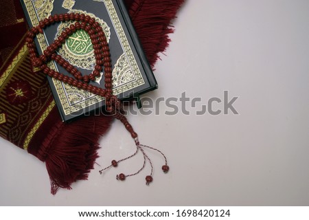 Composition with Holy Qur'an, red prayer beads and prayer rugs with a white background and space for the text.  Royalty-Free Stock Photo #1698420124