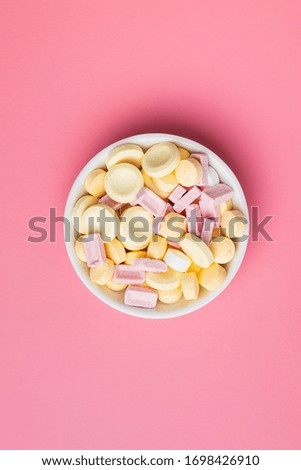 Mix of hard colorful candies in bowl on pink background. Top view.