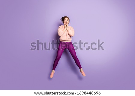Full length photo of pretty lady jumping up high excited mood look unbelievable low cool shopping prices wear casual fluffy stylish pullover pants isolated purple color background