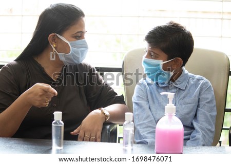 Cautious mother wearing face mask explaining her son how to use hand sanitizer to prevent infectious coronavirus disease  Royalty-Free Stock Photo #1698476071