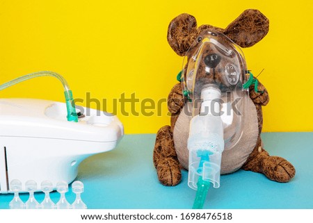 Coronavirus treatment concept. Funny dog with a medical face mask or nebulizer for treatment of the respiratory tract further five ampoules and a inhaler device on a blue table over yellow background.