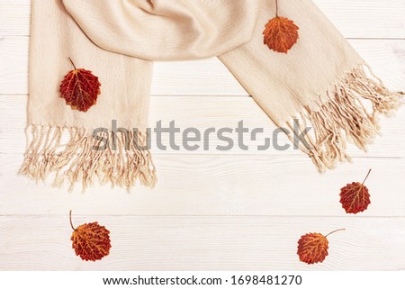 Autumn flat lay, red autumnal season leaves of aspen tree, fabric scarf on light wooden table with copy space. View from above.
