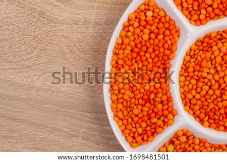 Orange lentils. Background texture of grains of orange lentils. Top view of dry lentils in a white plate. Close-up, horizontal, place for text. The concept of a healthy diet and agriculture.