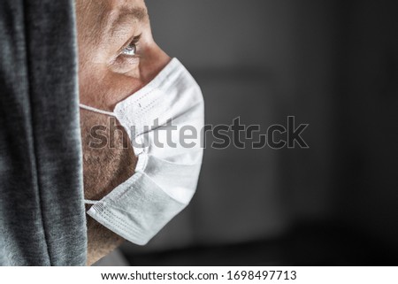 Young tired man in a hood and a medical mask look up with hope, on a dark background. Copy space. Close-up portrait in profile. Concept, World pandemic coronavirus. Stop the coronavirus epidemic