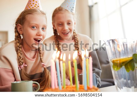 Portrait of excited girl in party hat celebrating birthday together with her sister they eating birthday cake at home