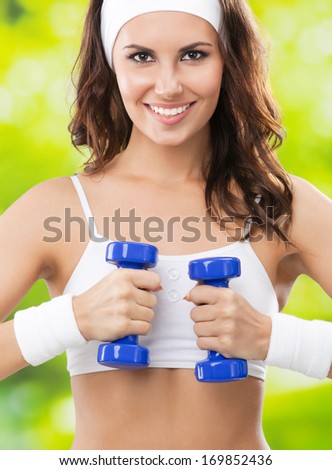 Portrait of cheerful woman in fitness wear exercising with dumbbell, outdoors