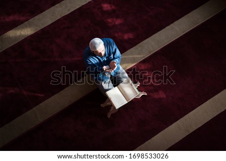 Young Arabic Muslim man reading Koran and praying. Religious muslim man reading holy koran inside the mosque. Royalty-Free Stock Photo #1698533026