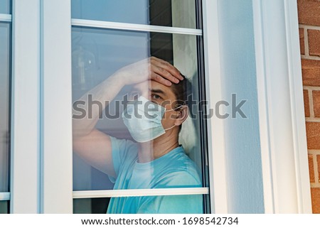 COVID-19. Sick man of coronavirus looking through the window and wearing mask protection and recovery from the illness in home. Quarantine isolation COVID19. Sick isolated at home to prevent infection Royalty-Free Stock Photo #1698542734