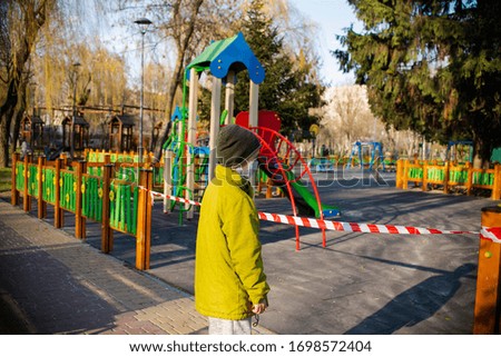 
it is impossible on a playground a child a boy stands on the background of a playground surrounded by a protective tape and the virus cannot enter the epidemic