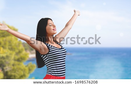 Happy young woman with hands raised on sea background
