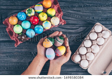 Flat lay easter eggs in egg cartoon with man_s hands full of eggs on dark wooden background. horizontal