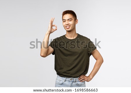 No problem, leave it to me. Satisfied and confident, assertive young asian man standing relaxed and carefree, wink encourage friend, show okay sign guarantee best quality, recommend service