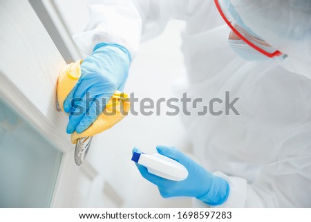 Disinfection and cleaning door handles of house from infection with virus and microbes in biochemical suit. Coronavirus protection concept. Royalty-Free Stock Photo #1698597283