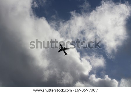 Picture of a plane flying in the sky, with large fluffy clouds in the background