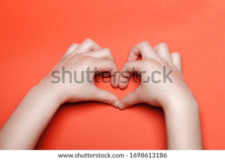 Child make a heart on a red background.