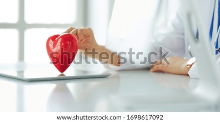 Female doctor with stethoscope holding heart, on light background