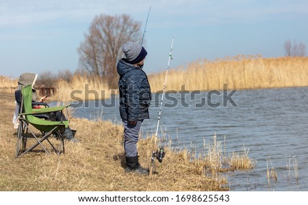 The boy catches fish in the lake for fishing rod. Early spring