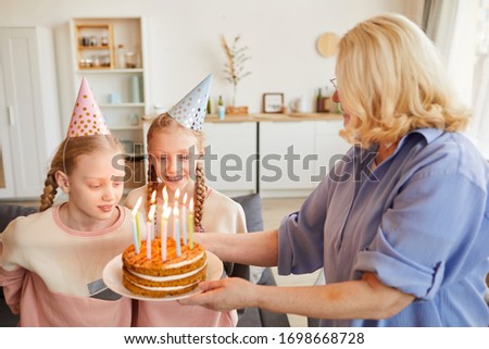 Grandmother cooking birthday cake with candles for her granddaughters they celebrating birthday at home