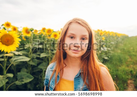 Outdoor portrait of cute young red-haired girl posing in sunflower field