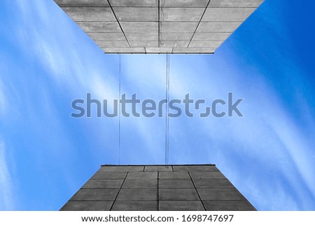 Abstraction of a blue sky with white clouds between the two walls of a gray house. View from below. Background and texture
