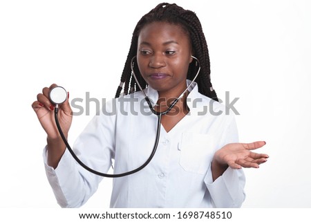 Female american african doctor, nurse woman wearing medical coat and using stethoscope. Confused, excited for success medical worker posing on light background isolated