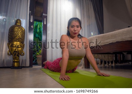 yoga against lockdown quarantine stress - young beautiful and happy Asian Chinese woman doing yoga workout at home bedroom practicing relaxation and meditation exercise in healthy lifestyle