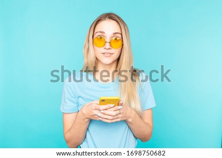 Young woman with mobile phone over isolated blue background surprised looking at the camera