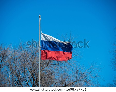 A developing Russian flag on a flagpole against a background of autumn trees and a blue sky.