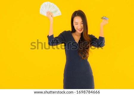 Portrait beautiful young asian woman with cash and credit card on yellow isolated background
