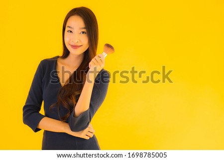 Portrait beautiful young asian woman with makeup brush on yellow isolated background