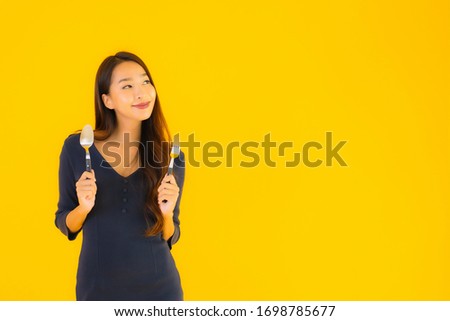 Portrait beautiful young asian woman with spoon and fork ready for eat on yellow isolated background