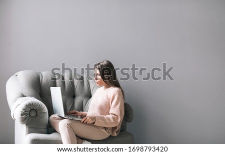 Beautiful young woman sits in an armchair and works at a laptop. Freelancer, distant work.