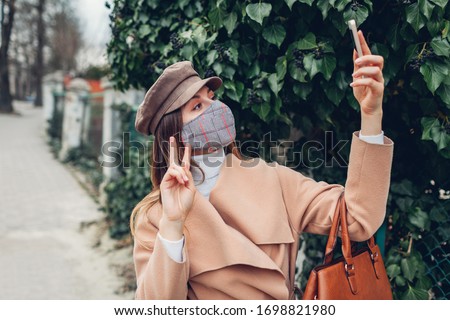 Woman wears reusable hand made mask outdoors during coronavirus covid-19 pandemic. Girl taking selfie on phone on empty street. Stay safe. Spring fashion