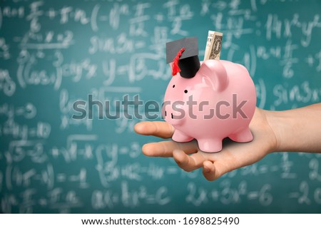 Pink piggy bank with black graduation hat on a human hand Royalty-Free Stock Photo #1698825490
