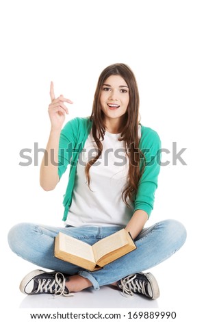 Young beautiful woman student sitting with book and pointing up. Isolated on white.