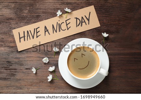 Delicious coffee, flowers and card with HAVE A NICE DAY wish on wooden table, flat lay. Good morning