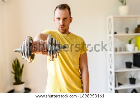 Make your shape better. Put yourself in order by the summer. The guy holds an iron dumbbell in his hand, he demonstrates it to the camera. Concept of a healthy lifestyle and strength workout at home
