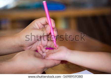 Closeup hands. Mother used to hold the pink magic pen, drawing, painting art on the skin of the daughter's hand. Education with stay at home concept.
