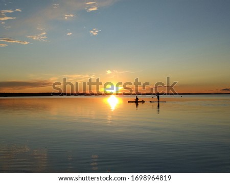 Beautiful sunset on Lake Pleshcheevo in Russia. On a smooth surface of the water, two people swim on a SUP-boards