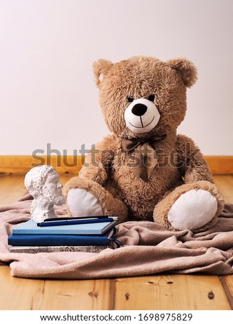 A teddy bear sitting next to a stack of books, writing set and plaster bust
