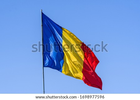 Romanian national flag blowing in the wind in direct sunlight towards clear blue sky
