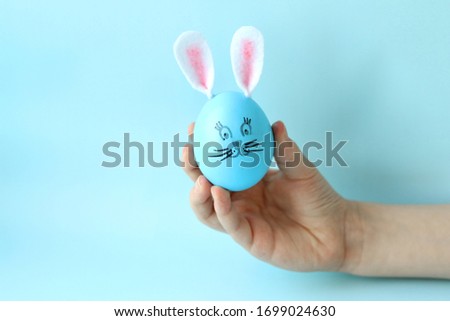 A blue Easter egg decorated with felt ears and a painted rabbit face in the child's hand. Easter bunny. Selective focus