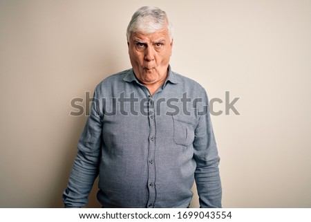 Senior handsome hoary man wearing casual shirt standing over isolated white background making fish face with lips, crazy and comical gesture. Funny expression.